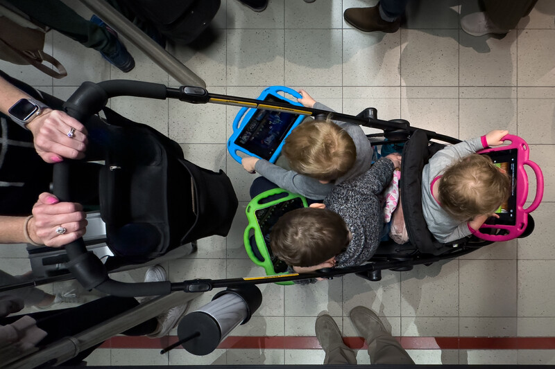 Overhead view of three young children in strollers viewed from above on a tiled floor.