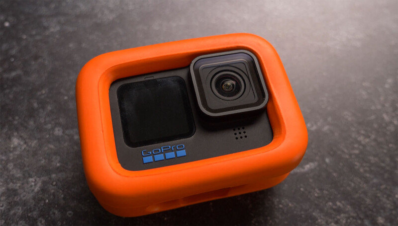 GoPro Hero 11 action camera with bright orange protective floating case on textured gray surface.