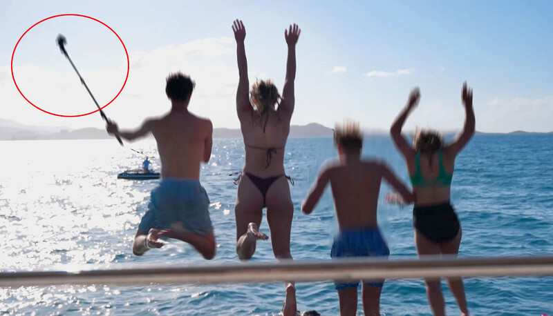 Four people in swimwear jumping in shallow ocean water with arms raised, one holding a brush circled in red.