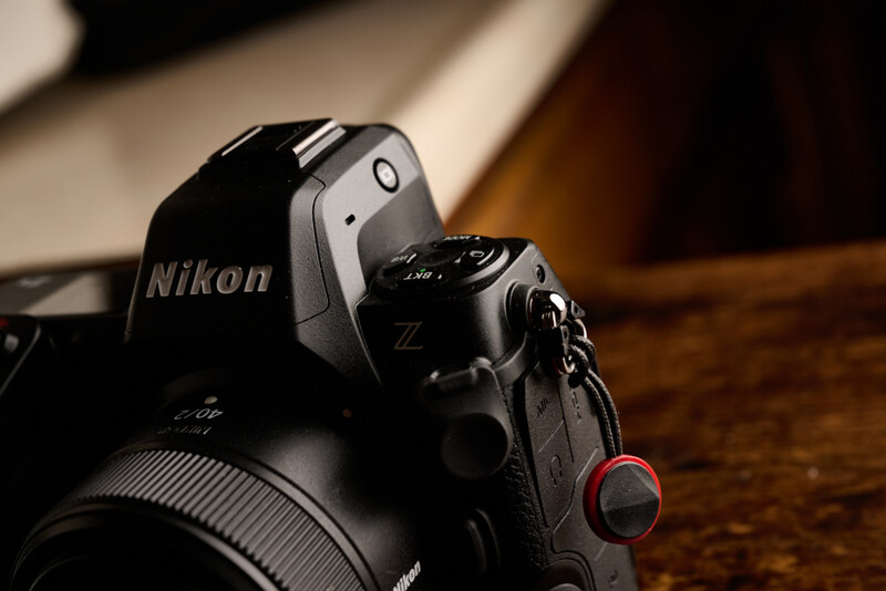 Nikon Z mirrorless camera with attached compact camera, positioned on wooden surface with warm studio lighting.