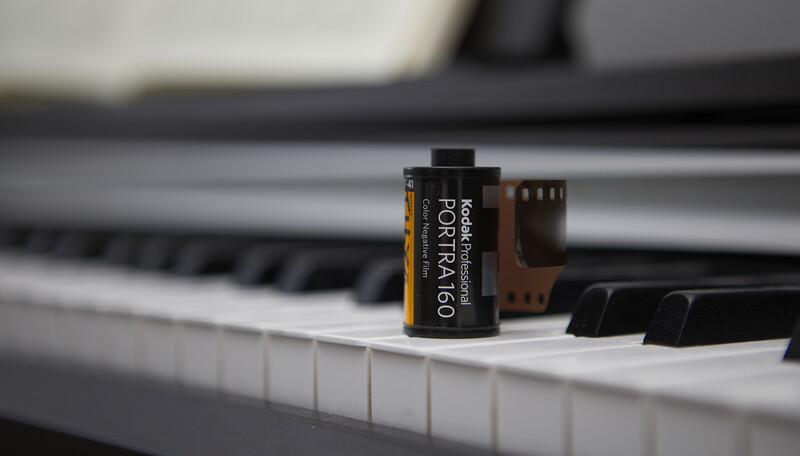 Kodak Portra 160 film canister positioned on piano keys with blurred keyboard in background.