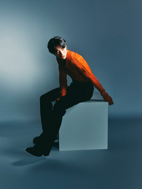 Person in orange jacket perched on white cube against blue gradient background.