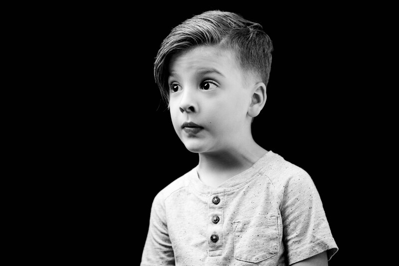 Young boy in profile against black background, wearing gray henley shirt.