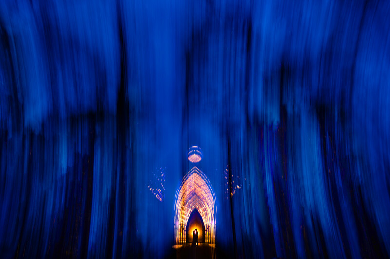 Gothic cathedral interior with glowing golden arched doorway framed by blue vertical light streaks.