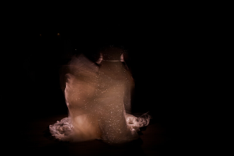 Close-up portrait of a person's face and shoulders against a black background with golden particles or dust scattered across the skin.