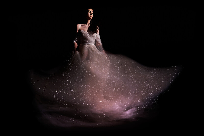 Woman in sparkly off-shoulder gown with dramatic skirt against black background.
