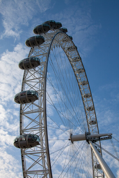 The London Eye observation wheel photographed from below against a bright blue sky with wispy clouds.