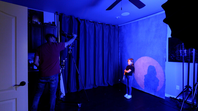 Studio setup with blue ambient lighting, camera on tripod, and silhouetted figure against projected circular light.