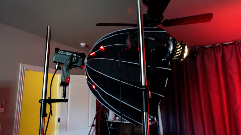 Professional softbox lighting setup with stand and reflector in studio environment with red curtains.