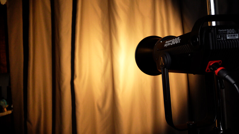 Professional video camera with red accents positioned against warm, glowing golden curtains in a studio setting.