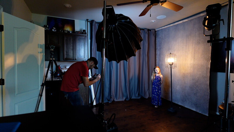 Professional studio setup with child model being photographed under controlled lighting with large reflector and key light.