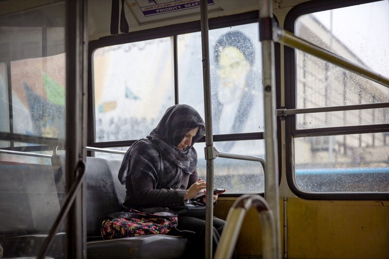 Person sitting alone on a public bus, looking at a phone, with frost-covered windows and blurred urban scenery.