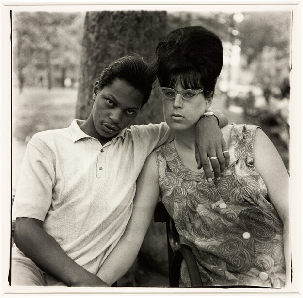 Two young people pose closely together outdoors in a black and white portrait.