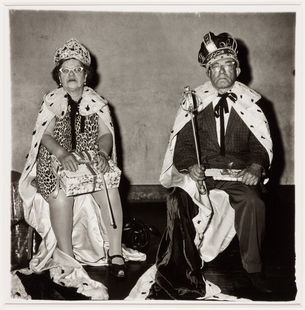 Two figures in formal royal regalia with ermine-trimmed robes and ornate crowns seated against a neutral backdrop.