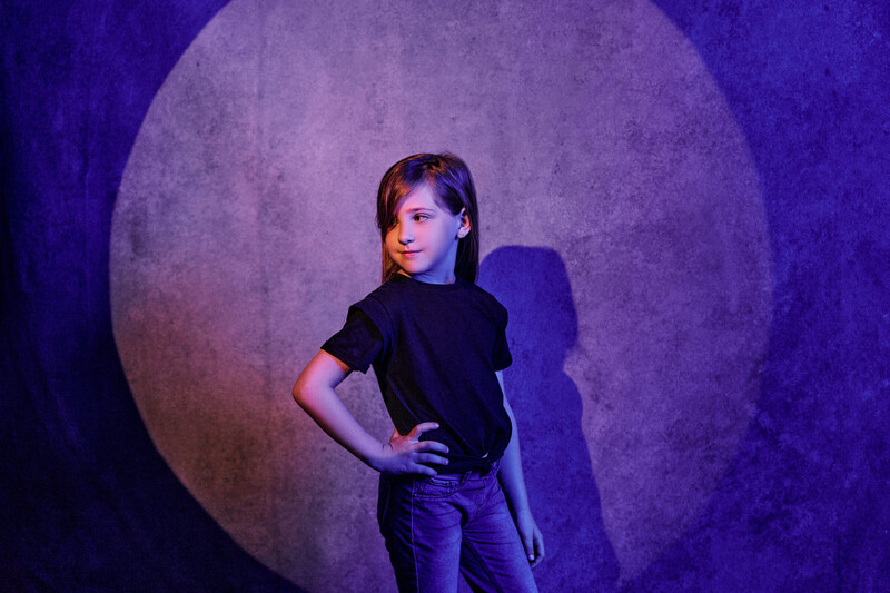 Young person in black shirt posing against a large circular light backdrop with purple atmospheric lighting.