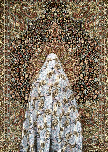 Person wearing an ornate white and gold patterned garment standing against an elaborate dark floral tapestry.