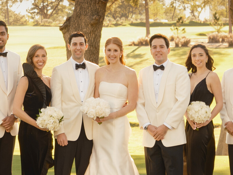 Wedding party of six people in formal attire standing outdoors beneath a large tree.