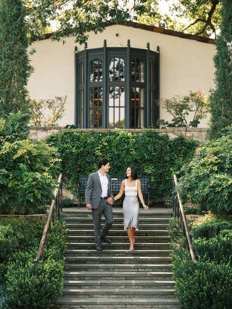 Couple walking down stone stairs lined with ivy toward an arched doorway with black doors.