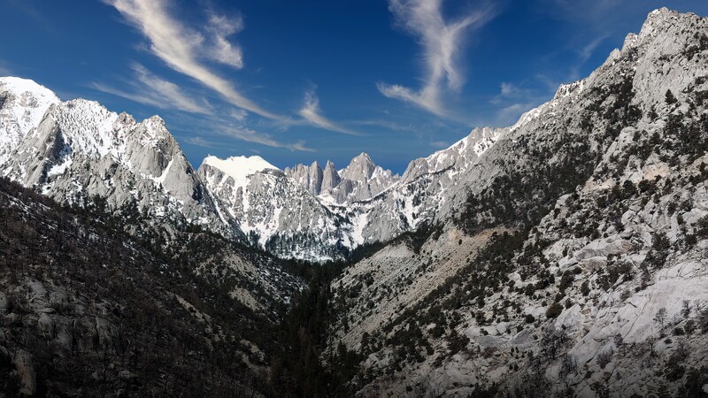 Snow-covered mountain peaks and forested slopes framing a distant valley under clear blue sky.