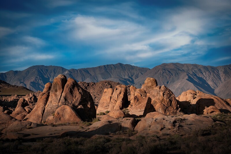 Towering rock formations in a desert landscape with mountains in the distant background under a blue sky.