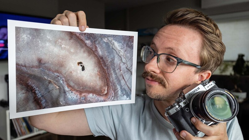 Photographer holding vintage rangefinder camera and displaying print of spiral galaxy with small silhouette figure.