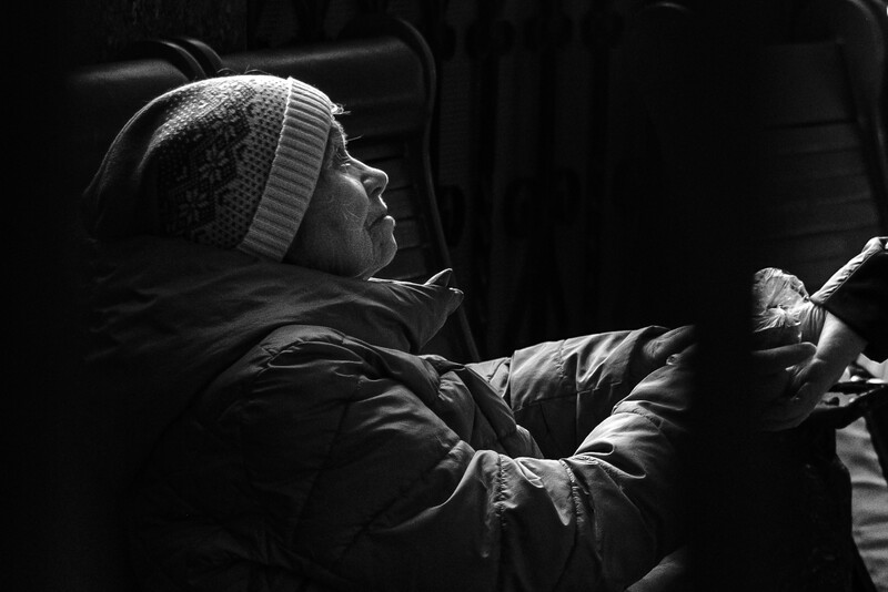 Person in winter beanie and puffy jacket shown in profile against dark background with dramatic side lighting.