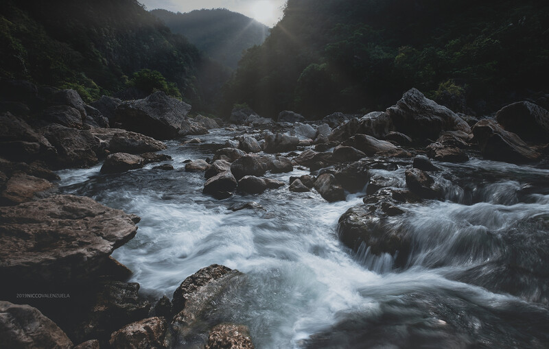 Mountain river flowing through a rocky gorge with mist and dense forest canopy.