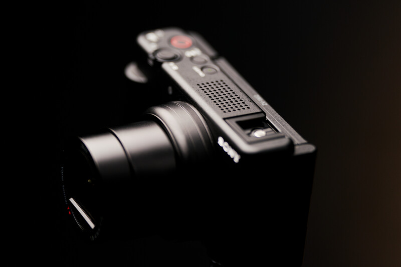 Compact camera with extended lens shown against a dark background in dramatic lighting.