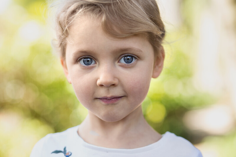 Young child with light brown hair and blue eyes looking directly at camera with slight smile.