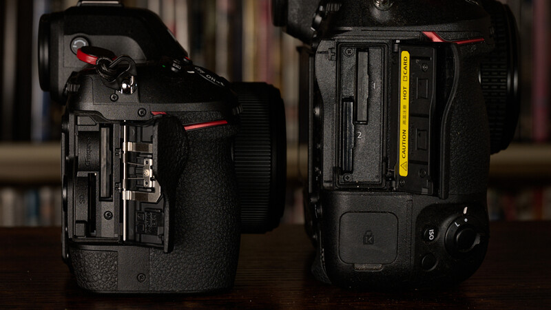 Rear view of two professional cinema cameras showing battery compartments and external connections side by side.