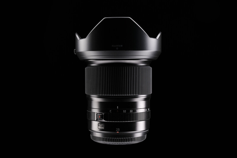 Wide-angle lens with hood mounted, displayed against black background with studio lighting.