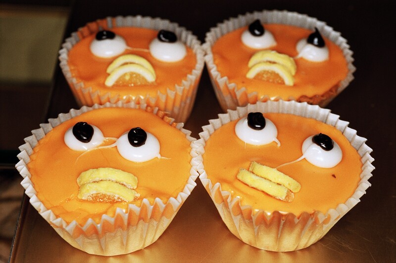 Close up image of 4 orange cupcakes with decorative expressionless faces added.