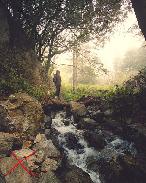 Hiker standing on rocks beside a flowing forest stream at golden hour