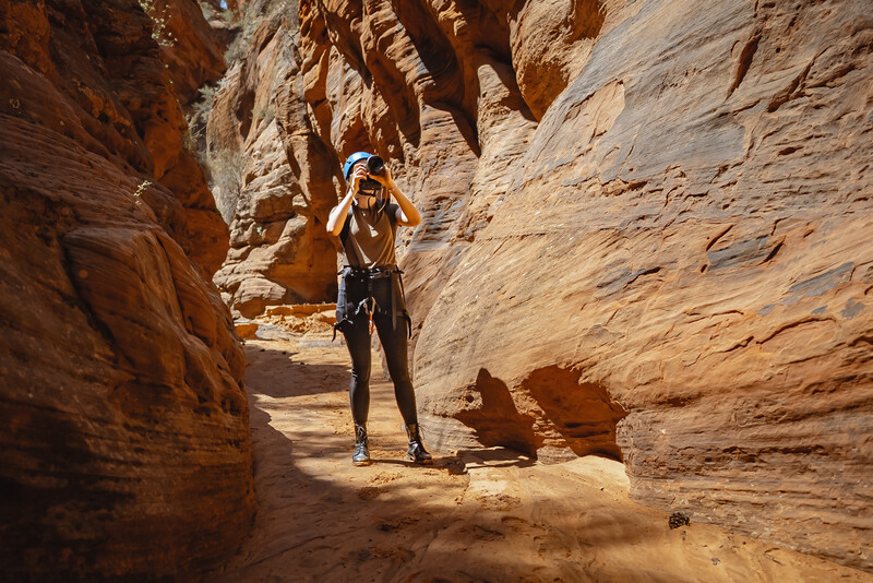 Trail runner ascending through a narrow sandstone canyon with warm, natural sunlight illuminating the rust-colored walls.