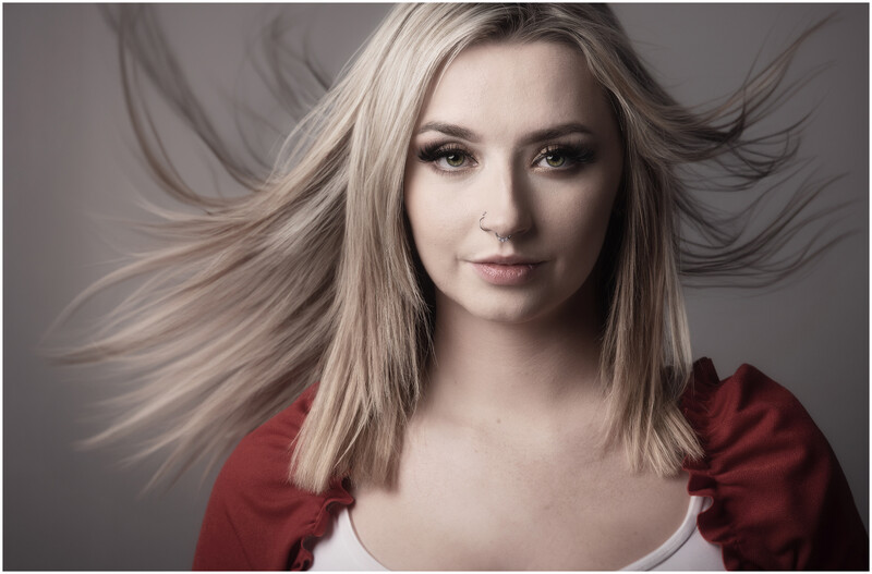 Portrait of a woman with long blonde hair wearing a red top against a neutral gray background.