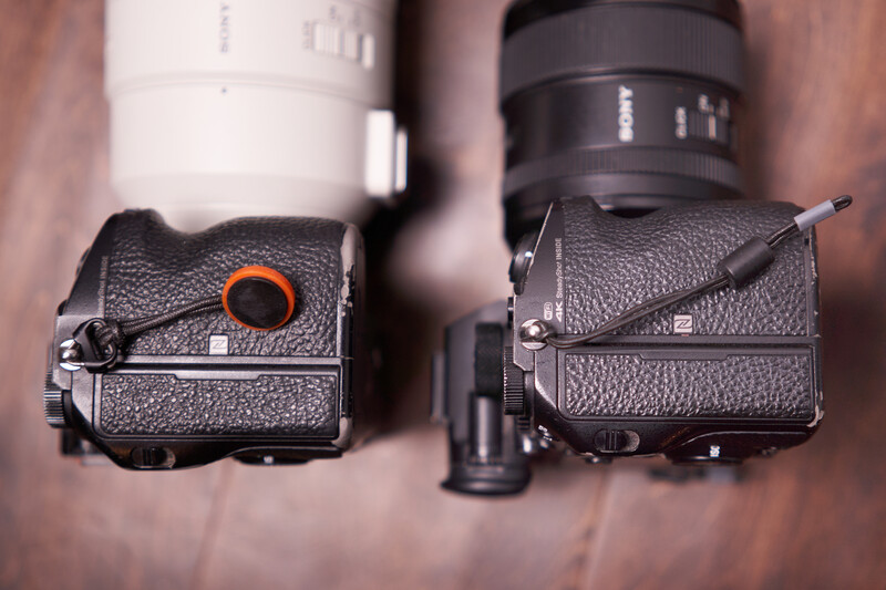 Two black camera bodies with textured grips positioned side by side, one featuring an orange accent ring, with lenses mounted above.