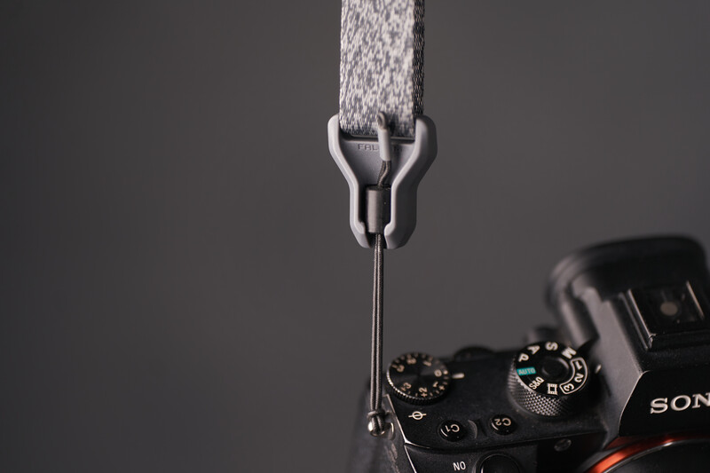 Water stream flowing through a metal showerhead positioned above a Sony camera body against a dark background.