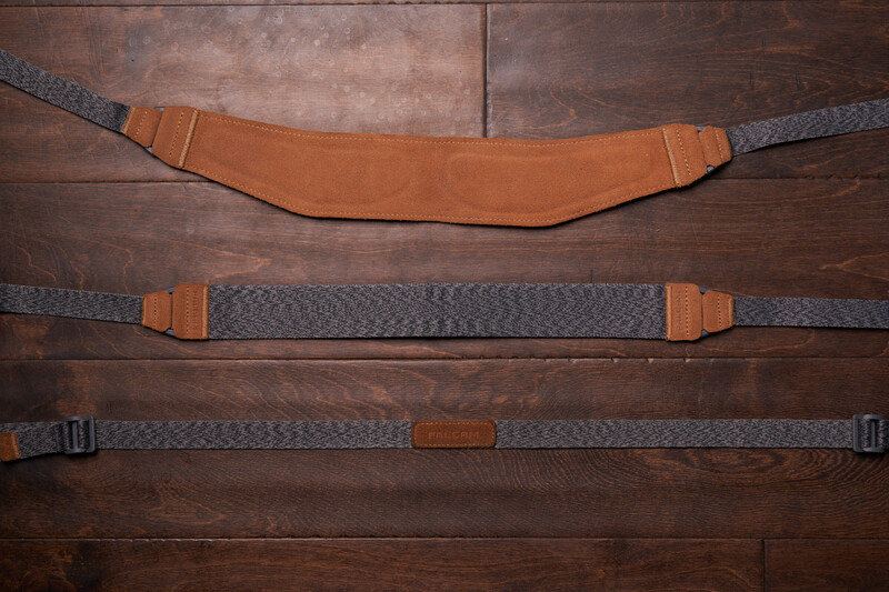 Three camera shoulder straps with leather and woven textile construction displayed flat on wood surface.