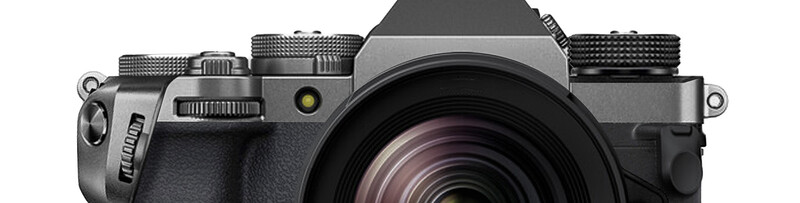 Top-down view of a mirrorless camera with silver body and black accents, showing lens, dials, and textured grip.