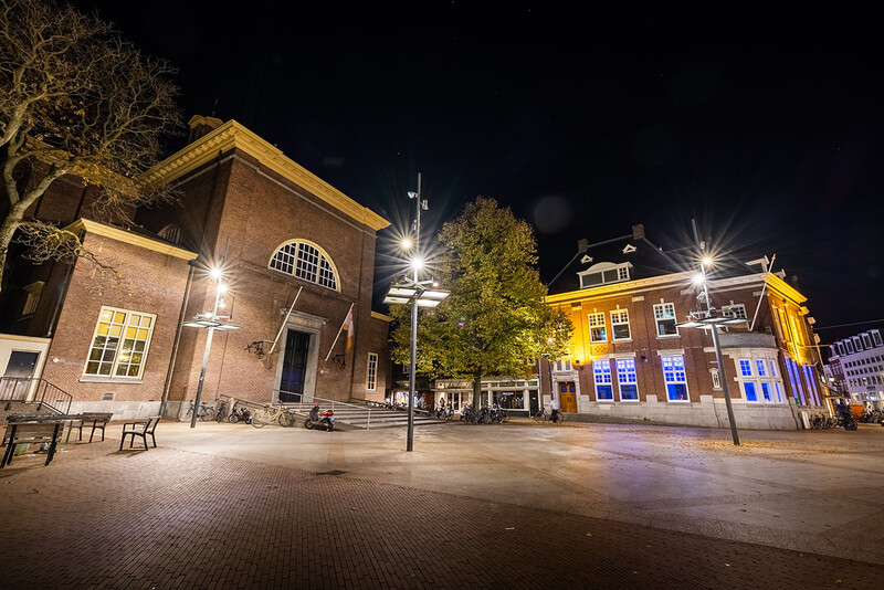 Nighttime architectural plaza with illuminated brick buildings and street lamps.