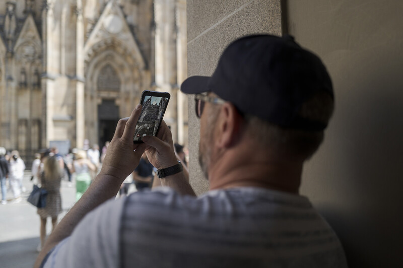 Person holding smartphone to photograph an ornate Gothic cathedral facade in bright sunlight.