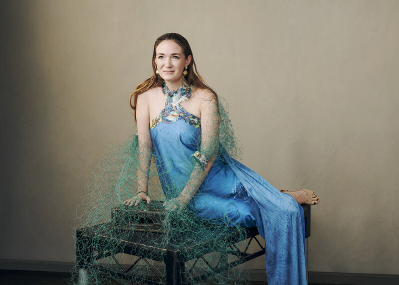 Woman in blue dress seated with sheer green fabric draped around her shoulders and fishing net prop.