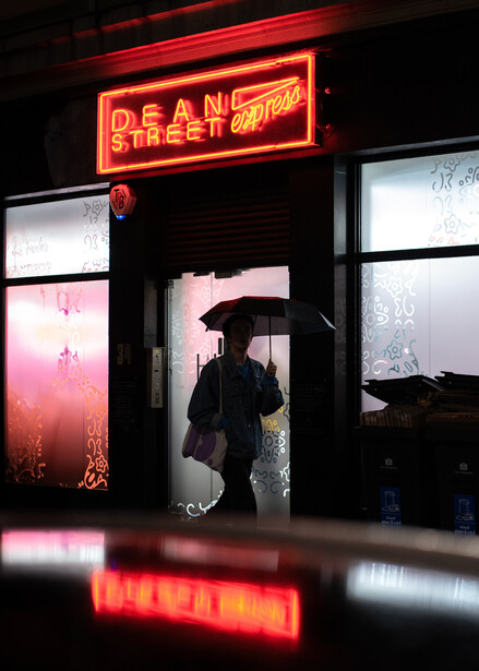 The same image of a person walking with an umbrella in the rain with the left side of the frame expanded, using Adobe Generative Fill