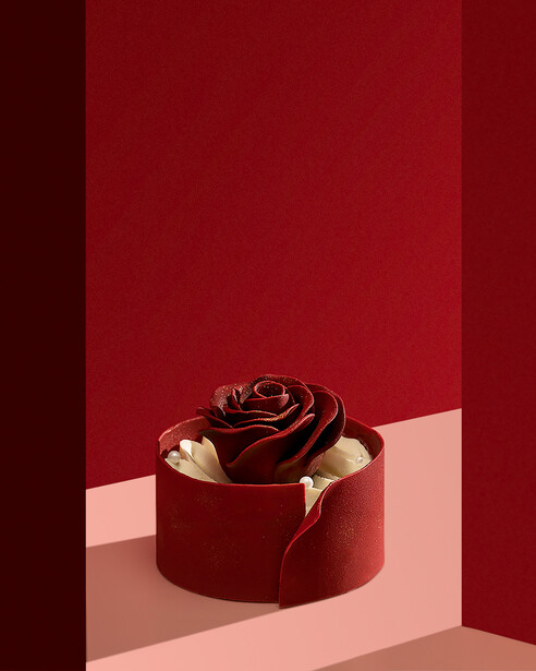 Deep red rose with gold leaf accents in a round velvet box, photographed against a minimalist background.