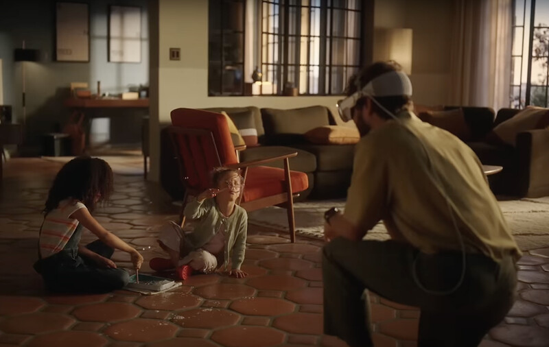 Adult and two children sitting on a terracotta tile floor in a modern living room with warm natural light.
