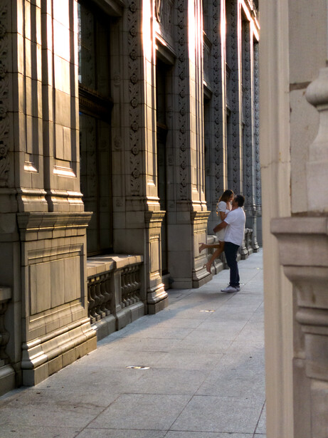 Person standing in a narrow European alleyway lined with tall ornate buildings featuring gold-trimmed dark facades.