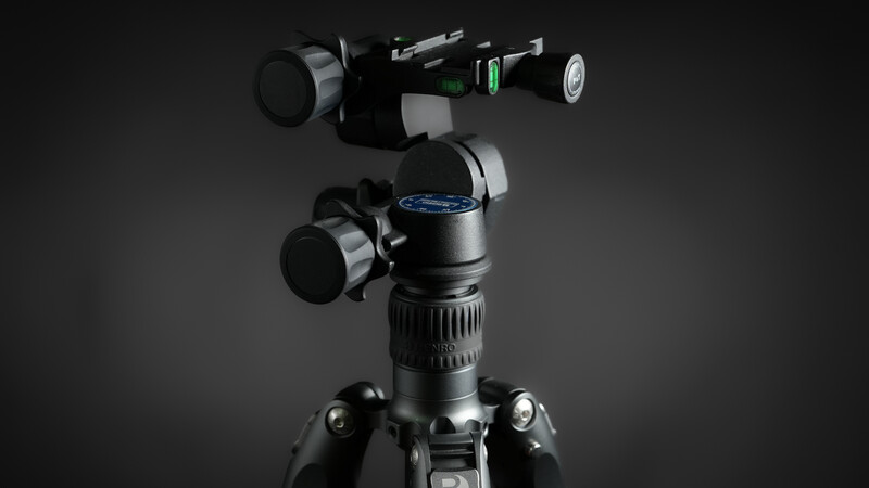 Professional video tripod head with dual pan-tilt handles and mounted camera on dark background.