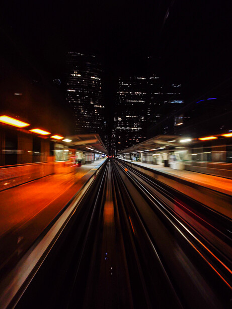 View from a moving train car down the center track toward city skyline at night with motion blur.