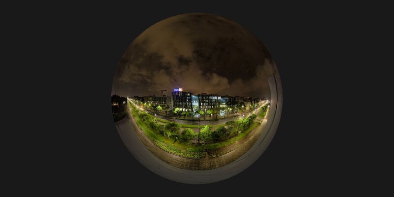 Night cityscape with illuminated buildings and green lawn viewed through a circular fisheye lens.