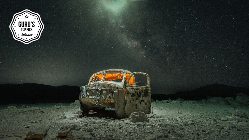 Abandoned and weathered truck cab under a starry night sky in an arid desert landscape.